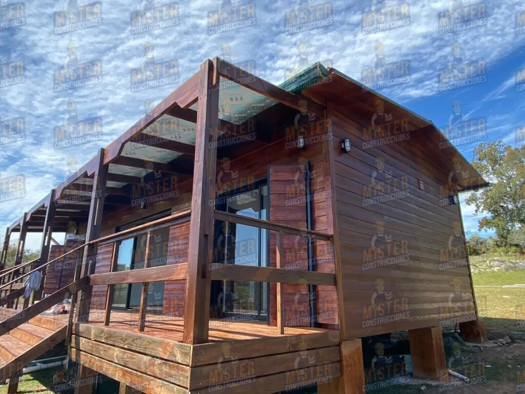 Casa contenedor elevada revestida en madera oscura, con terraza techada y escalera de acceso