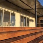 Fachada de casa contenedor con grandes ventanales, terraza de madera y estructura metálica en el techo