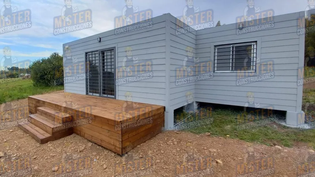 Fachada de casa contenedor gris con terraza de madera y escalón de acceso