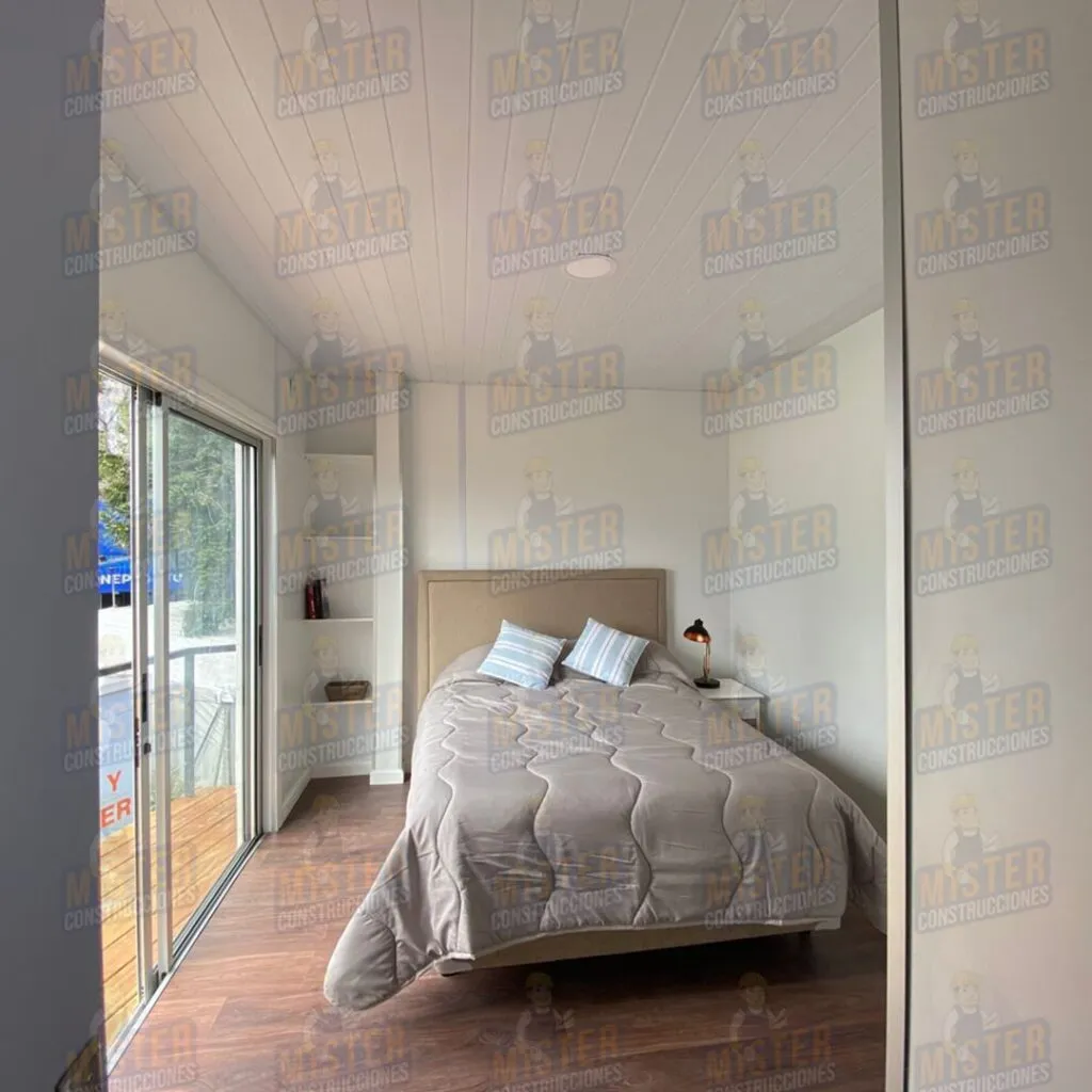 Interior de habitación en casa contenedor con cama matrimonial, mesita de noche y acceso a terraza a través de puerta corrediza