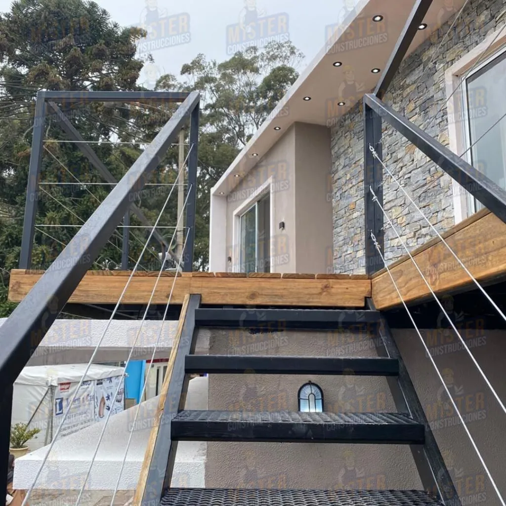 Escalera metálica con barandales de acero y madera, acceso a terraza de casa contenedor con revestimiento de piedra