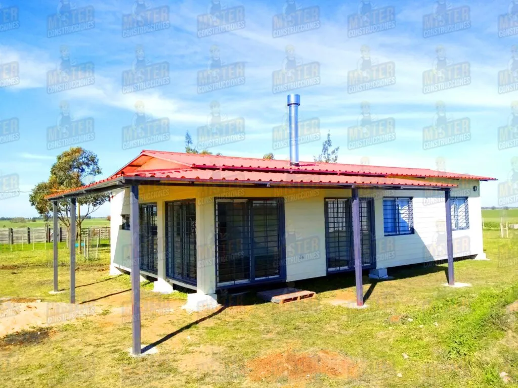 Casa contenedor con techo de metal rojo, chimenea visible, y estructura metálica en la terraza con ventanas protegidas por rejas