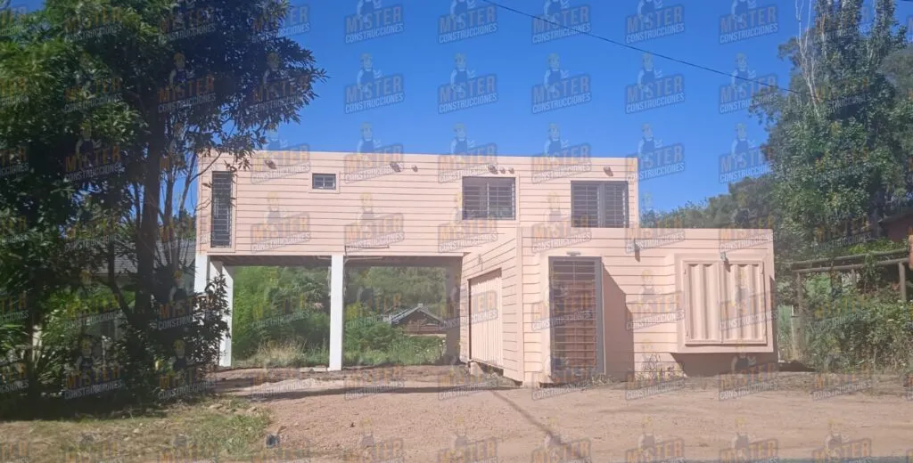Casa contenedor de dos plantas con diseño moderno y estructura elevada, rodeada de vegetación