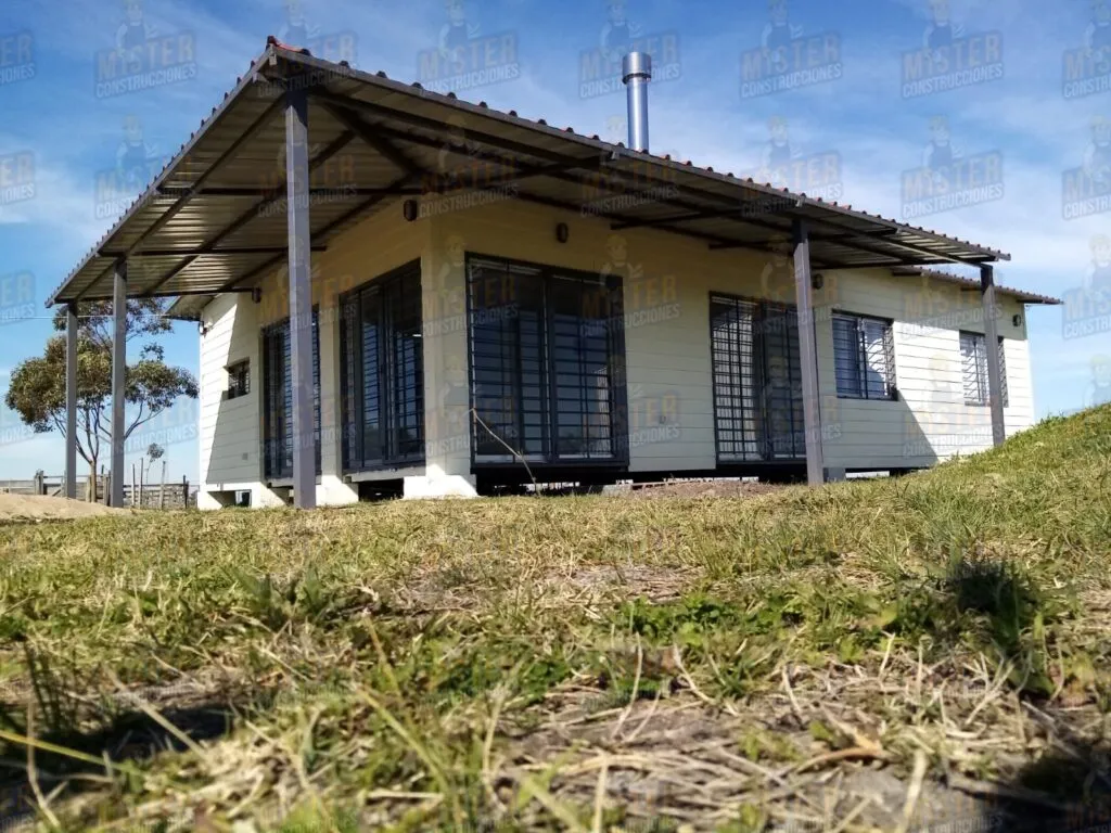 Casa contenedor con techo metálico, chimenea y grandes ventanas protegidas por rejas