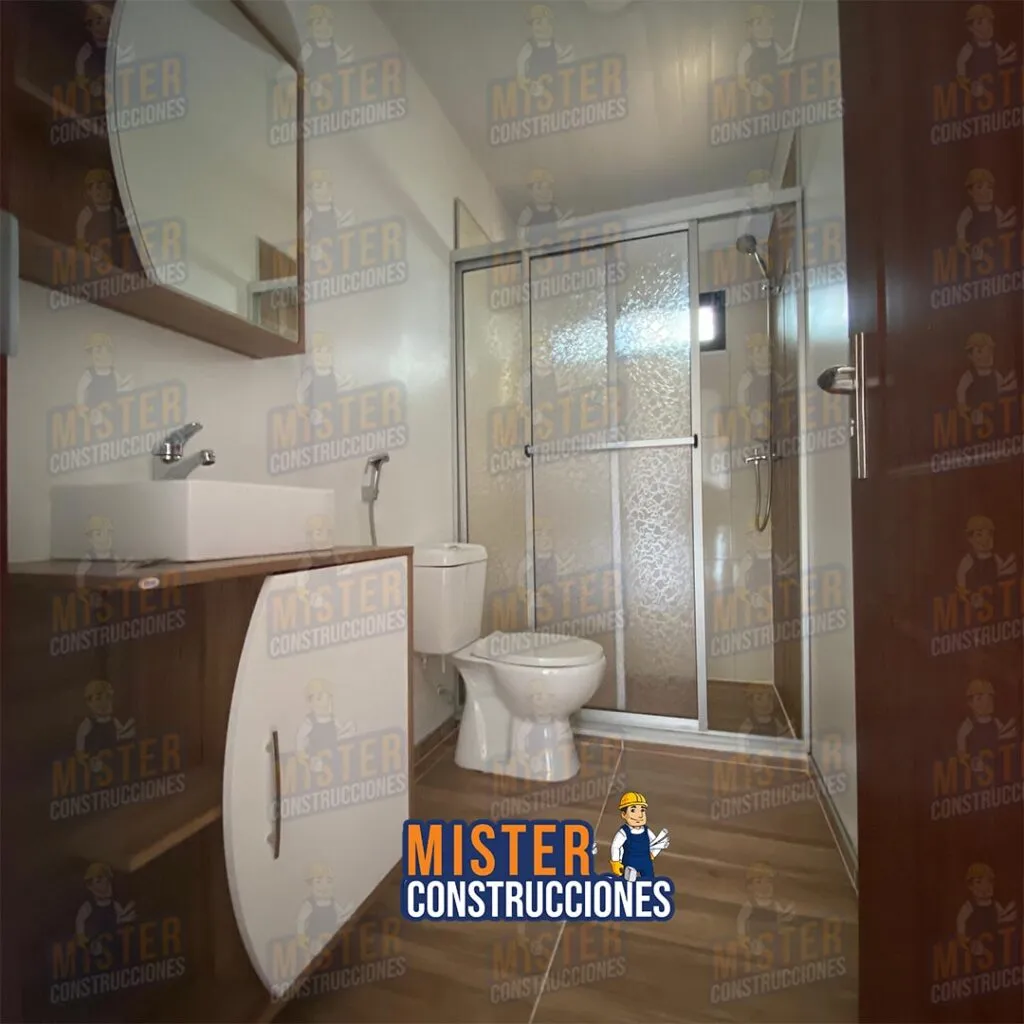 Baño moderno en casa contenedor de Mister Construcciones, con ducha con mampara, sanitario y mueble bajo lavamanos
