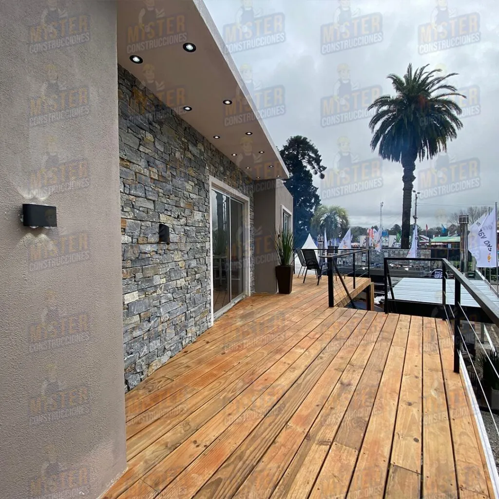 Fachada de casa contenedor con revestimiento de piedra, terraza de madera y vista a árboles