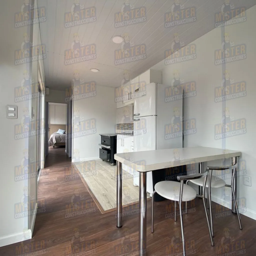 Interior de casa contenedor modular con mesa de comedor, cocina equipada y acceso a dormitorio