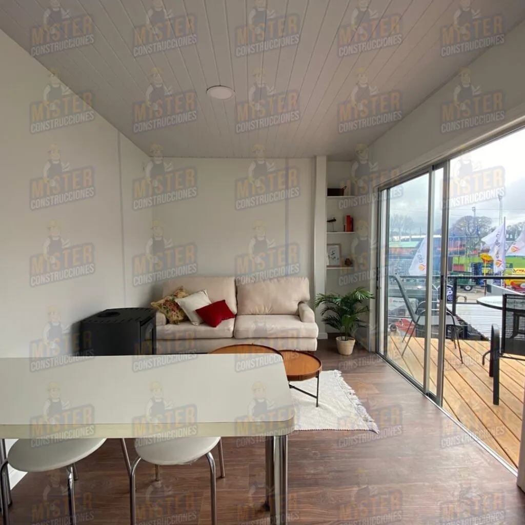 Interior de casa contenedor con living, sofá beige y vista al deck exterior de Mister Construcciones